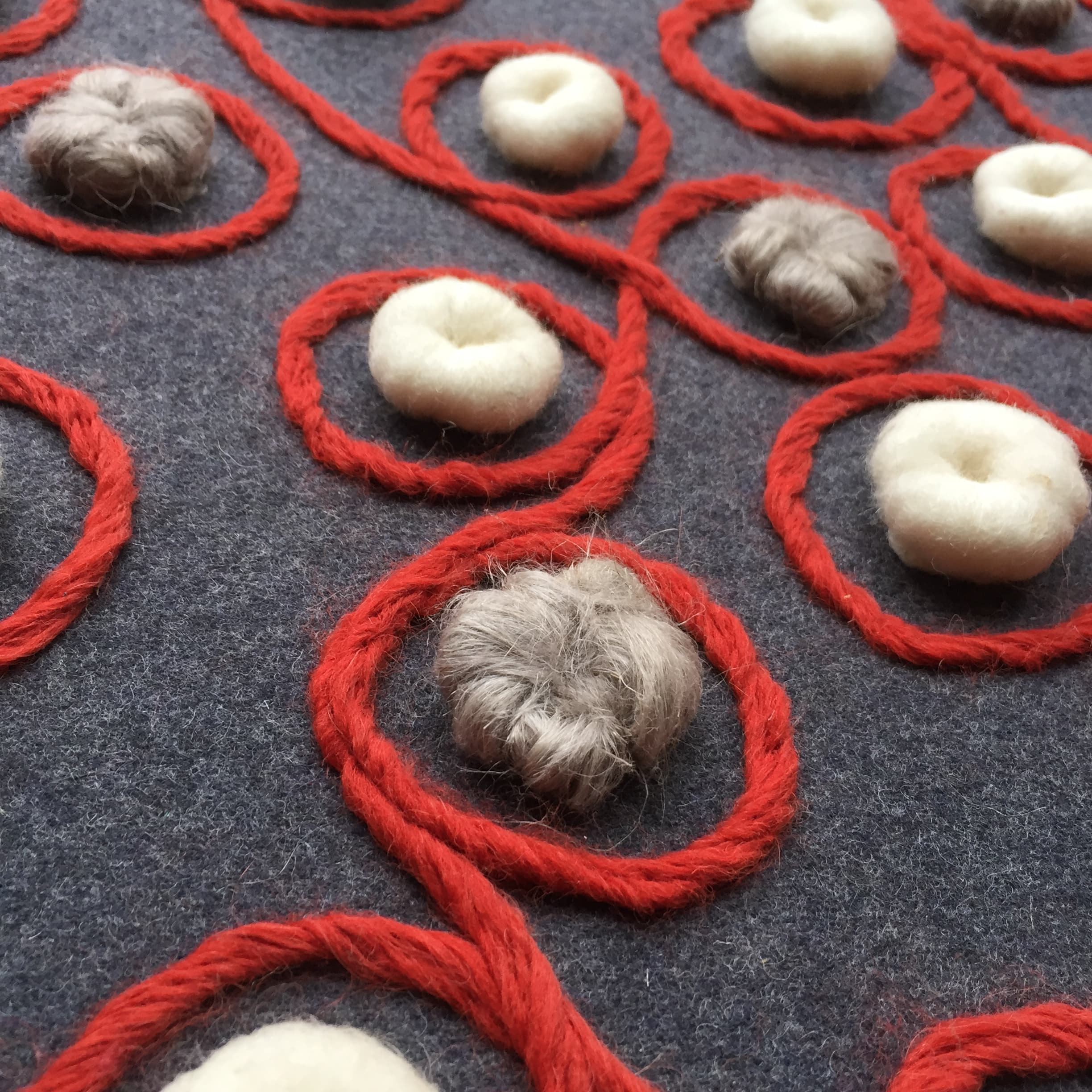 Detail of red yarn looping across grey felt with white wool accents
